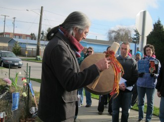 Photo from Seattle Neighborhood Greenways: Gene Tagaban of the Tlingit RavenCoho tribe plays a song for paddlers facing an important but difficult challenge at the site where James St. Clair was hit 