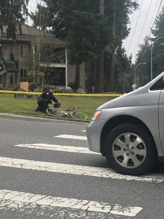 Photo of a police officer kneeling next to a bicycle on the side of the road.