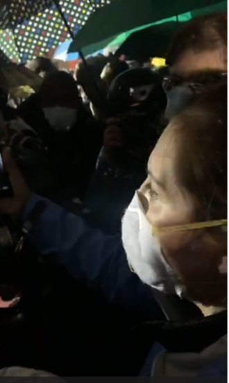Councilmember Teresa Mosqueda wearing a mask amid a large crowd of people recording a video on her phone.