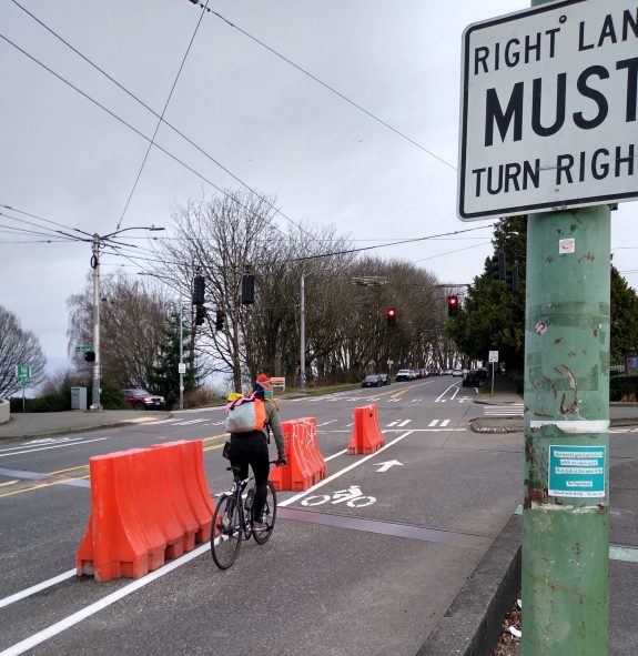 Bike rider in a lane with three large orange barriers protecting the bike lane that used to be a slip lane