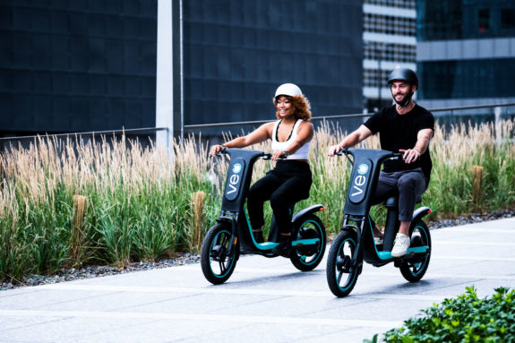 Promotional photo of two poeople riding Veo bikes on a path.