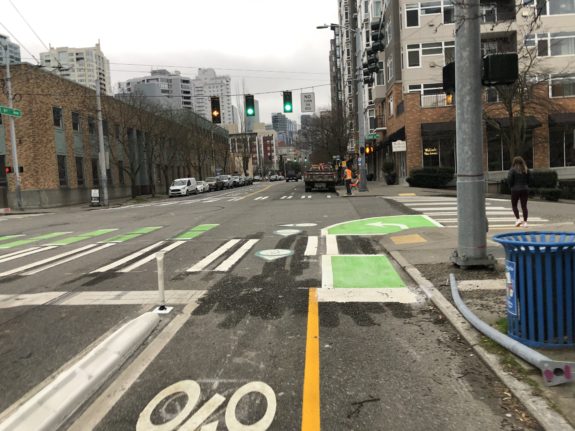 Photo of an intersection. A small green box is painted at the corner for people on bikes waiting to turn left.