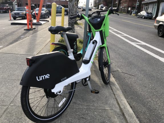 New white and green Lime bike parked next to a bike lane. 