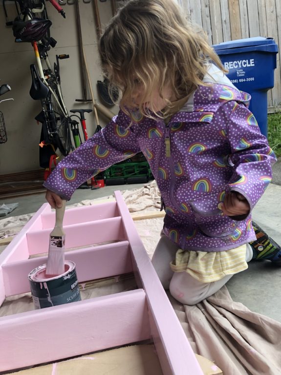 A kid painting a ladder pink.