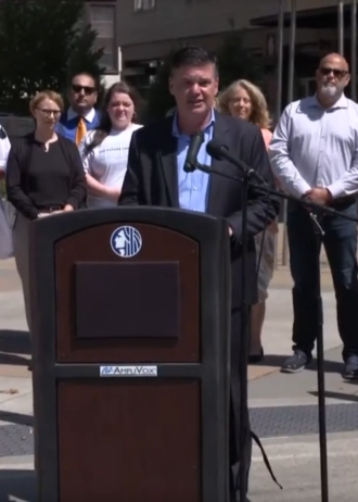 Screencapture showing Greg Spotts speaking at a podium.