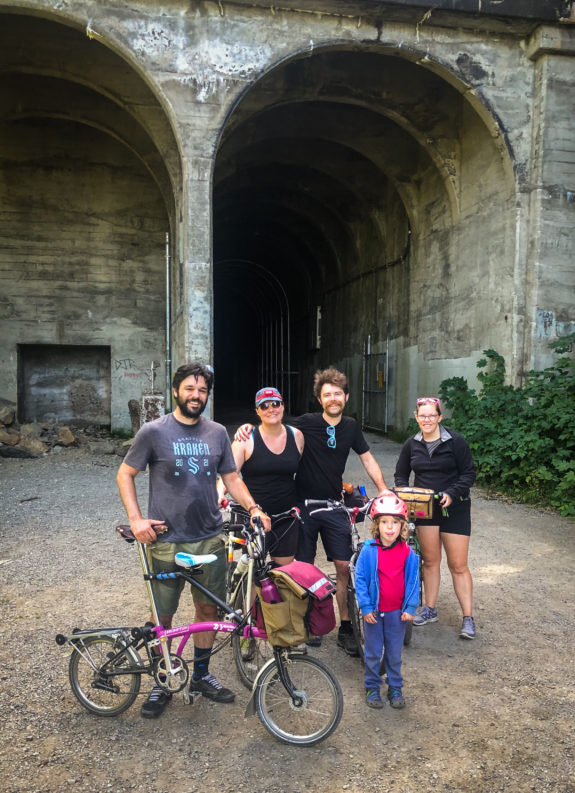 Four adults and a kid standing with bikes in front of the tunnel entrance.