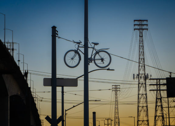 A ghost bike for Robb Mason hangs on a pole high in the air at sunset.