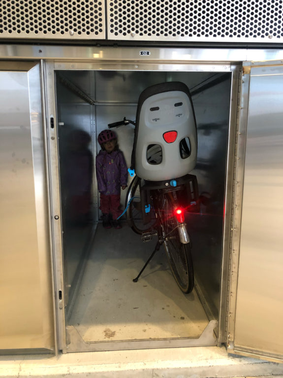 An open bike locker with a bicycle and child inside.