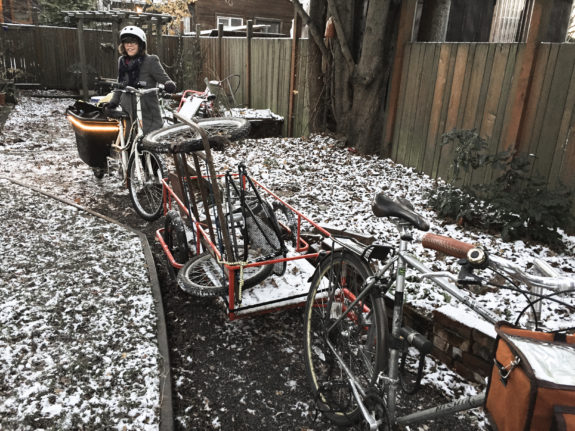 A woman with a cargo bike next to another bike with a trailer in the snow.