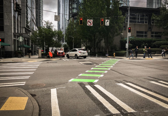 Photo of a green bike lane crossing diagonally through an intersection. 
