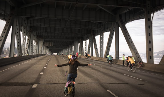 Person biking in the I-5 Express Lanes on the ship canal bridge with her arms out wide.