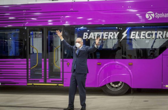 Governor Jay Inslee in front of a battery electric bus with his arms wide.