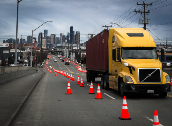 A truck passes a line of cones. Downtown Seattle is in the background.
