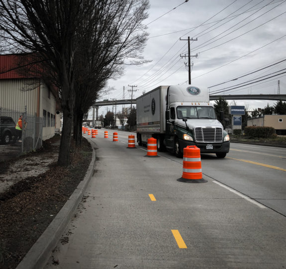 A truck passes next to some round barrels marking off the bike path.