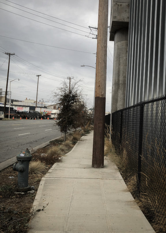 A sidewalk with a utility pole in the middle of it.