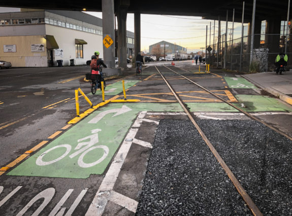 Person biking the wrong way rather than follow the city's intended route to cross the tracks. Yellow barriers direct people to make a sharp turn.