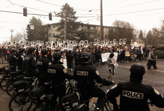 Seattle Police with bikes in the foreground watch a large crowd of marchers, many holding signs with MLK's face. 