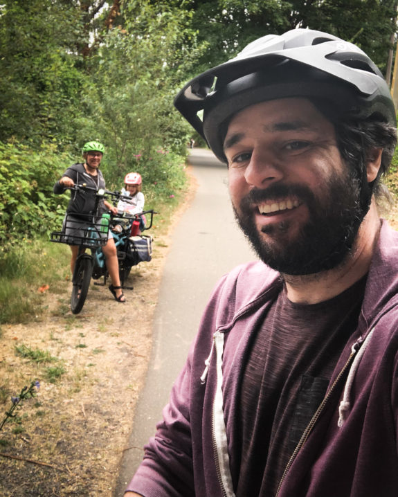 Selfie of the author with spouse Kelli and child on a cargo bike behind him on a trail.