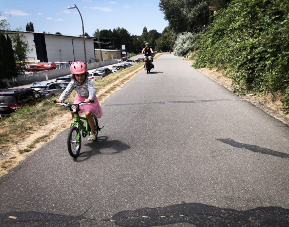A child with a pink helmet and pink tutu biking on a trail.