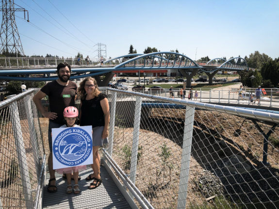 Photo of the author, spouse Kelli and child on the bridge holding a sign that says "Bridging Kirkland, Totem Lake Connector."