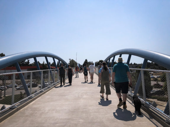 View from the bridge deck with a significant number of people walking on it and a wide open blue sky.