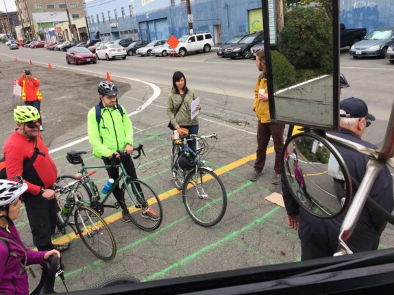 A group of people with bikes in a mock crosswalk as seen from the driver's seat of a large truck.