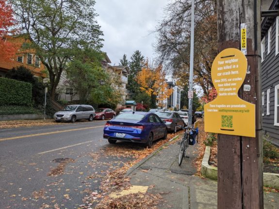 A yellow silhouette of a person's head is attached to a telephone pole with text, "Your neighbor was killed in a car crash here. Since 2015, car crashes have killed over 200 people on Seattle streets. These tragedies are preventable. Learn how. Seattle Neighborhood Greenways URL in post.