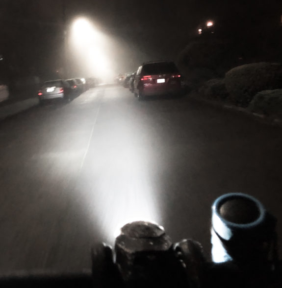 Photo from behind the handlebars at night. the headlight shines brightly.