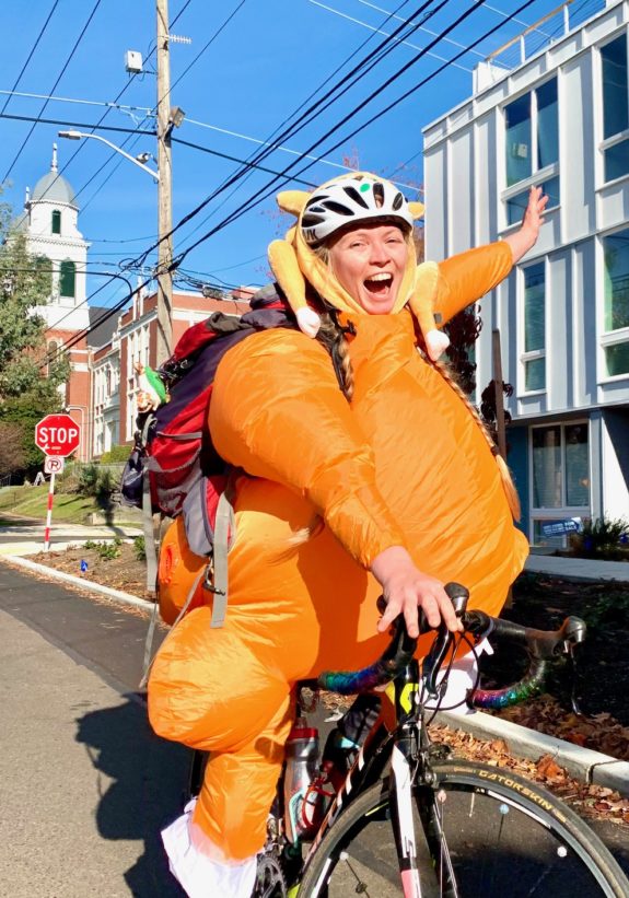 A person wearing a full-body blow-up turkey costume while riding a bike.